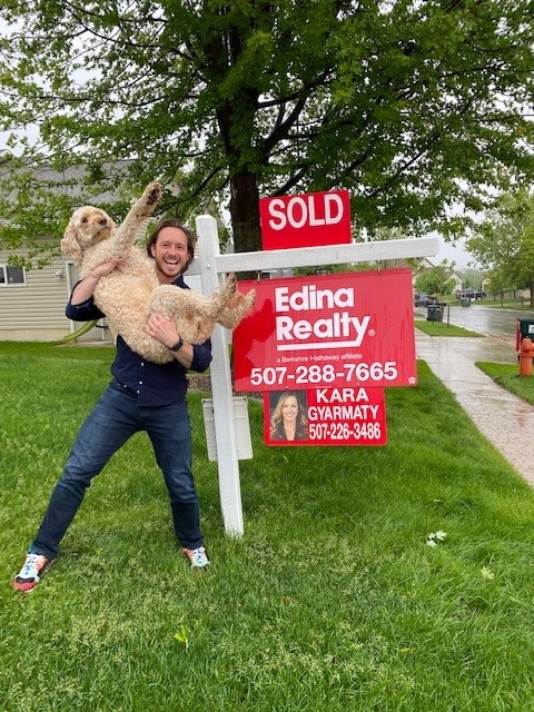 Guy with holding dog by Real Estate sold sign